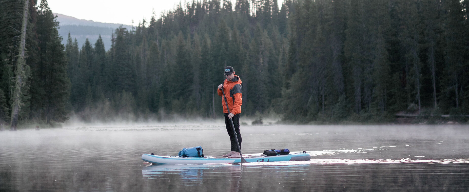 Man wearing a orange jacket paddle boarding on a lake